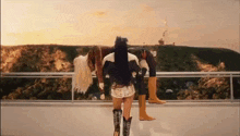 a group of women wearing cowboy boots are standing on a balcony overlooking a mountain .