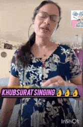 a woman wearing glasses and a blue floral dress is singing