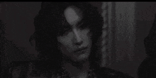 a black and white photo of a young man with long hair in a room .