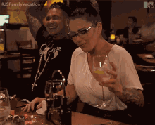 a man and a woman are sitting at a table with a glass of wine in front of them with the hashtag #jsfamilyvacation