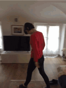 a woman in a red shirt is walking in front of a television