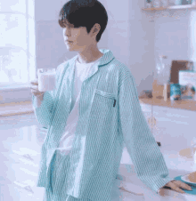 a man in a green and white striped shirt is leaning on a counter holding a glass of milk .