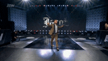 a man in a suit stands on a stage in front of a sign that says iron