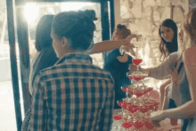 a woman in a plaid shirt is pouring a drink into a pyramid of glasses