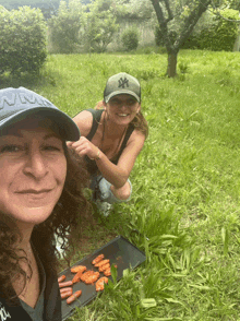 a woman wearing a ny hat sits next to another woman in a field