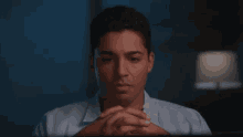 a man with his hands folded looks at the camera with a sad look on his face