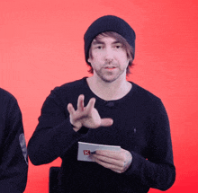 a man wearing a black sweater and a black beanie is holding a piece of paper that says k on it