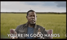a man is sitting in a chair in front of a field and giving a thumbs up .