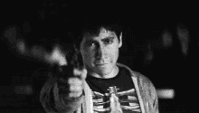 a black and white photo of a man wearing a skeleton shirt giving the middle finger .