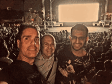 three men are posing for a picture in front of a crowd at a concert with a large screen that says " titanic " on it