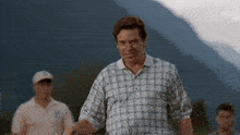 a man in a plaid shirt is standing on a golf course with a mountain in the background .