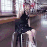 a woman in a black dress is sitting on a chair with her legs crossed and giving a peace sign .