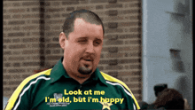 a man is wearing a green and yellow shirt that says look at me i 'm old but i 'm happy