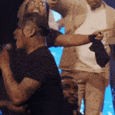 a man in a black shirt is singing into a microphone while another man points at him