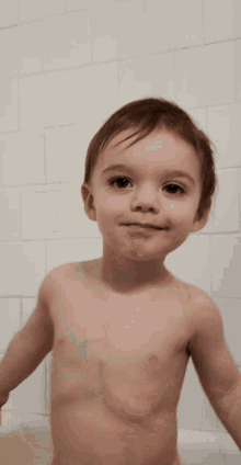 a young boy without a shirt is standing in a bathtub