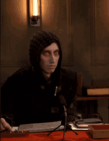 a man in a hooded jacket sits at a table with a microphone in front of him