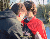 a man in a red cape is talking to another man who is wearing a black jacket