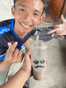 a boy wearing a shirt that says apex is holding a cup of coffee