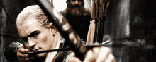 a man with long hair is holding a bow and arrow in his hand .