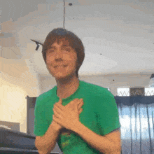 a man in a green shirt is holding his hands to his chest