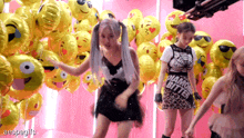 two girls are dancing in front of balloons with emojis on them