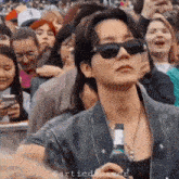 a man wearing sunglasses is standing in a crowd holding a bottle of beer .