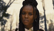 a woman with dreadlocks and a bow tie is standing in a forest .