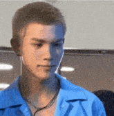 a close up of a young man wearing a blue shirt and a necklace .