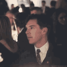 a man in a suit and tie is sitting in a crowd of people