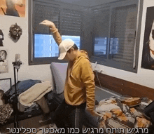 a man wearing a white hat is dancing in front of a window in a messy room