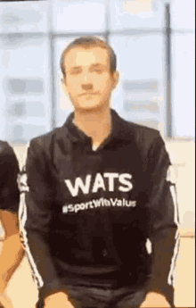 a man wearing a wats sweatshirt is sitting down with his eyes closed .