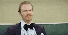 a man with a mustache wearing a purple suit and black bow tie
