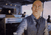 a bald man in a suit and tie is standing in front of a screen that says 1a