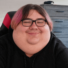 a young man with glasses and pink hair is smiling with his eyes closed