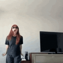 a woman wearing sunglasses and a black shirt is standing in front of a television in a living room .