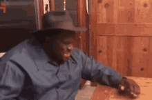 a man wearing a cowboy hat and a blue shirt is sitting at a table
