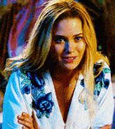 a blonde woman wearing a white shirt with blue flowers on the sleeves