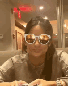 a woman wearing sunglasses has a reflection of a building in them