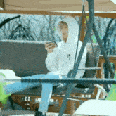 a person in a white hoodie is sitting on a swing looking at a cell phone .