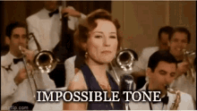 a woman singing into a microphone in front of a band with the words impossible tone written below her .