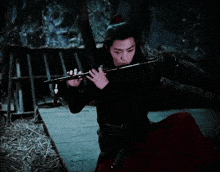 a man in a red dress is playing a flute in a dark room