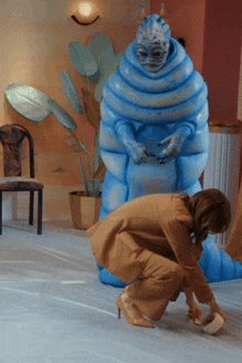 a woman kneeling down in front of a statue of a blue monster