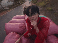 a man in a red dress is sitting on a pile of pink bags
