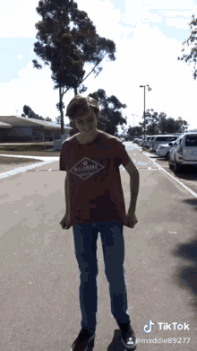 a young man wearing a red billabong t-shirt stands on a street