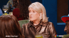 a woman in a sequined jacket is sitting at a table with other people and a nbc logo on the bottom