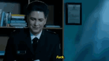 a man in a suit and tie says fuck in front of a bookshelf