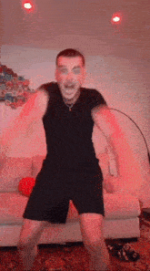a man in a black shirt and shorts is dancing in a living room with red lights .