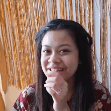 a woman with a ring on her finger smiles in front of gold tinsel