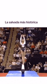 a female gymnast is doing a trick on a balance beam in front of a crowd ..
