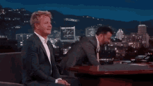 two men in suits are sitting at a table eating food .